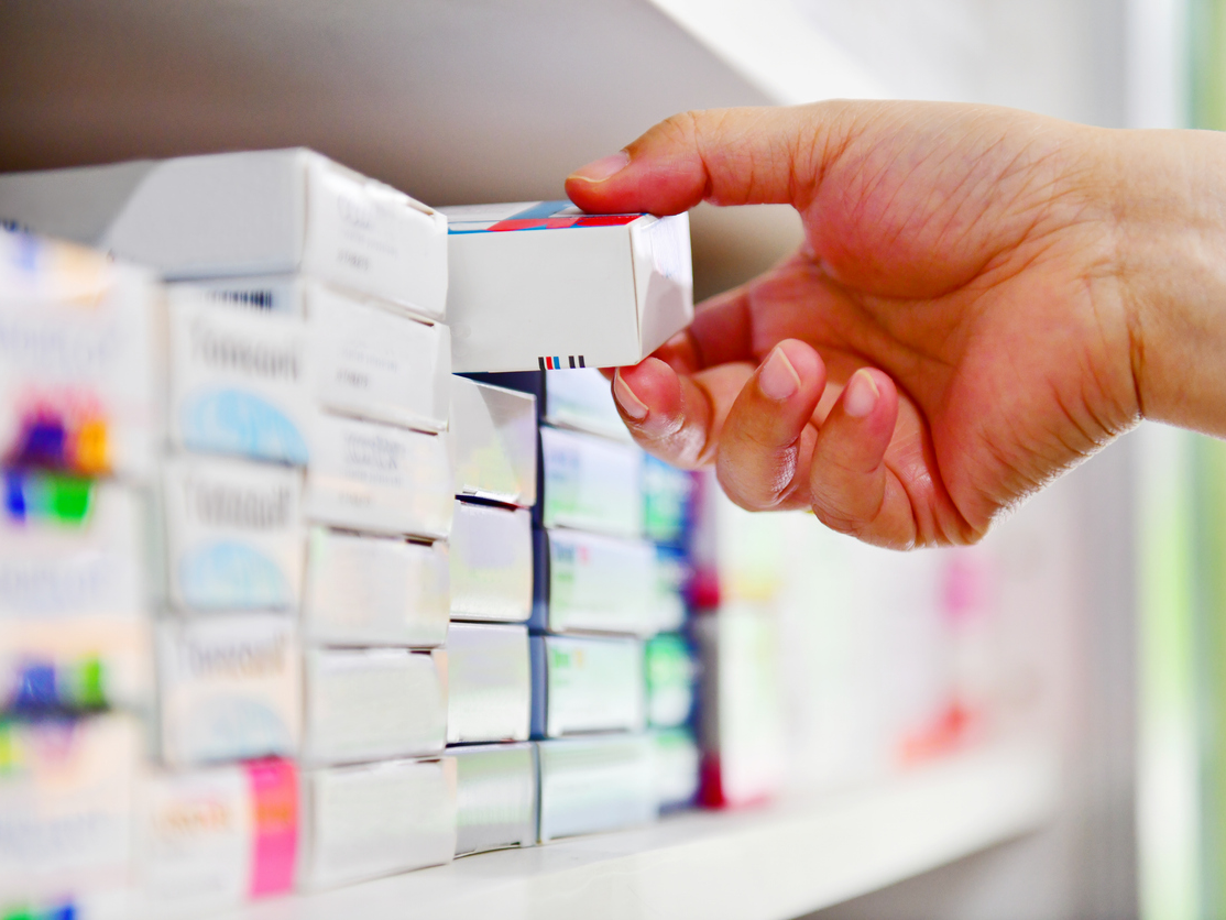 Una mà sosté una capsa de pastilles de la prestatgeria d'una farmàcia.