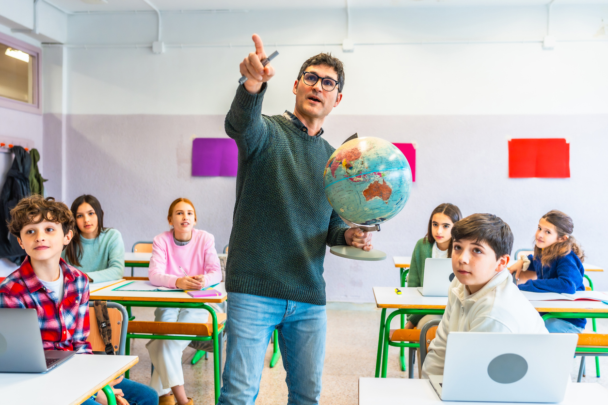 Un professor amb un globus terraqui, a una classe amb nins i nines.