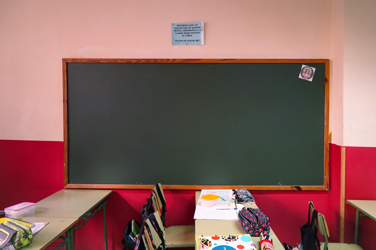 Una aula amb una pissarra i taules amb material escolar.