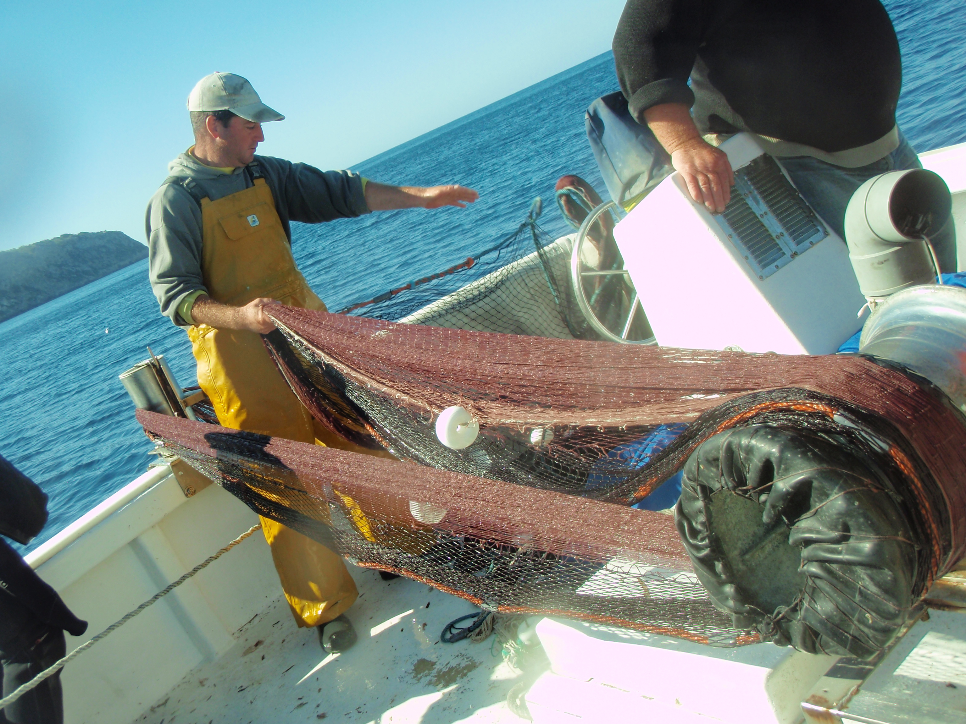 Un pescador recull la xarxa a un vaixell